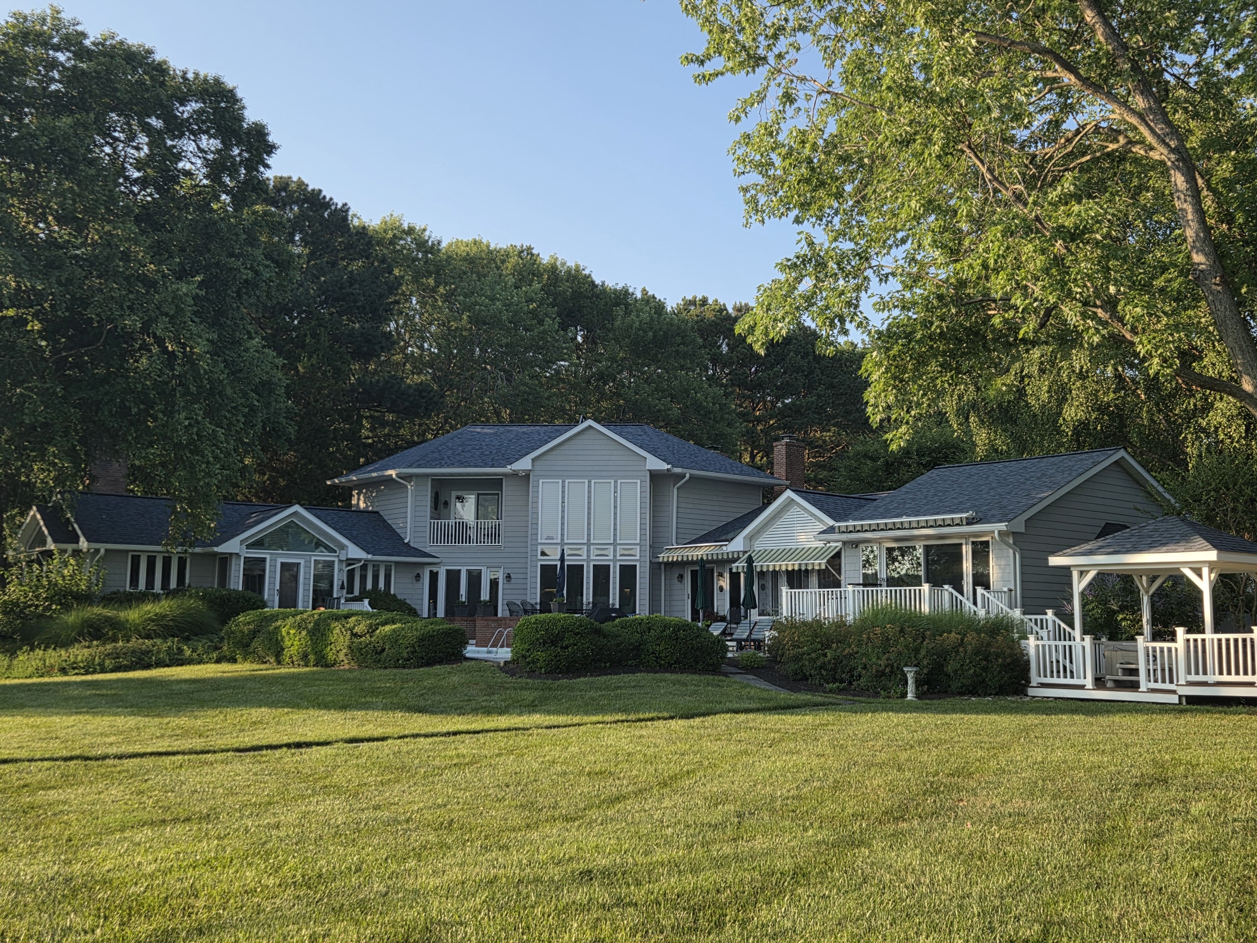 Wide view of a waterfront home with a newly completed dark roof system and manicured lawn